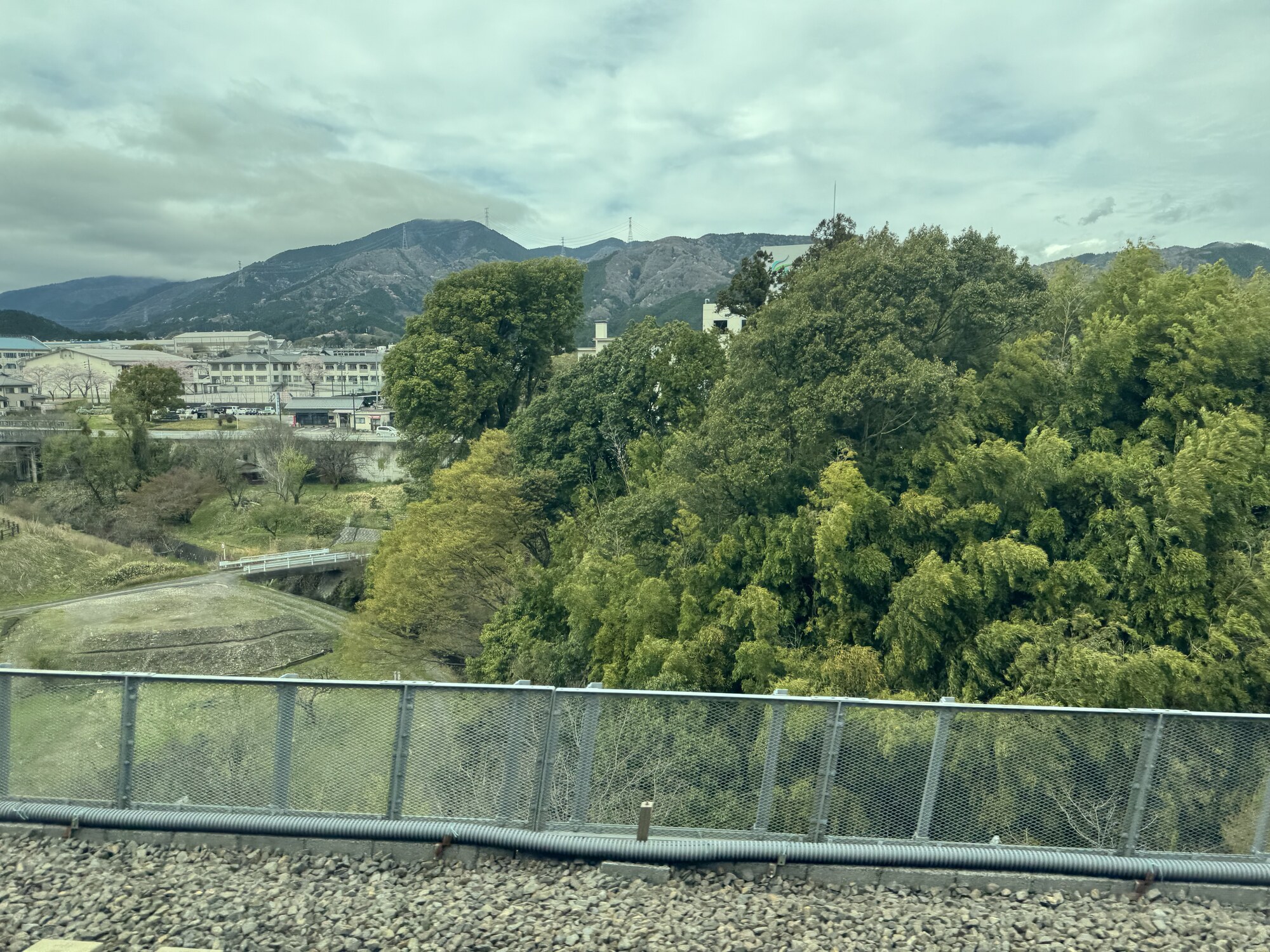 Widok z okna Shinkansena — dolina z polami i zabudową, w tle zalesione wzgórza, błękitne niebo