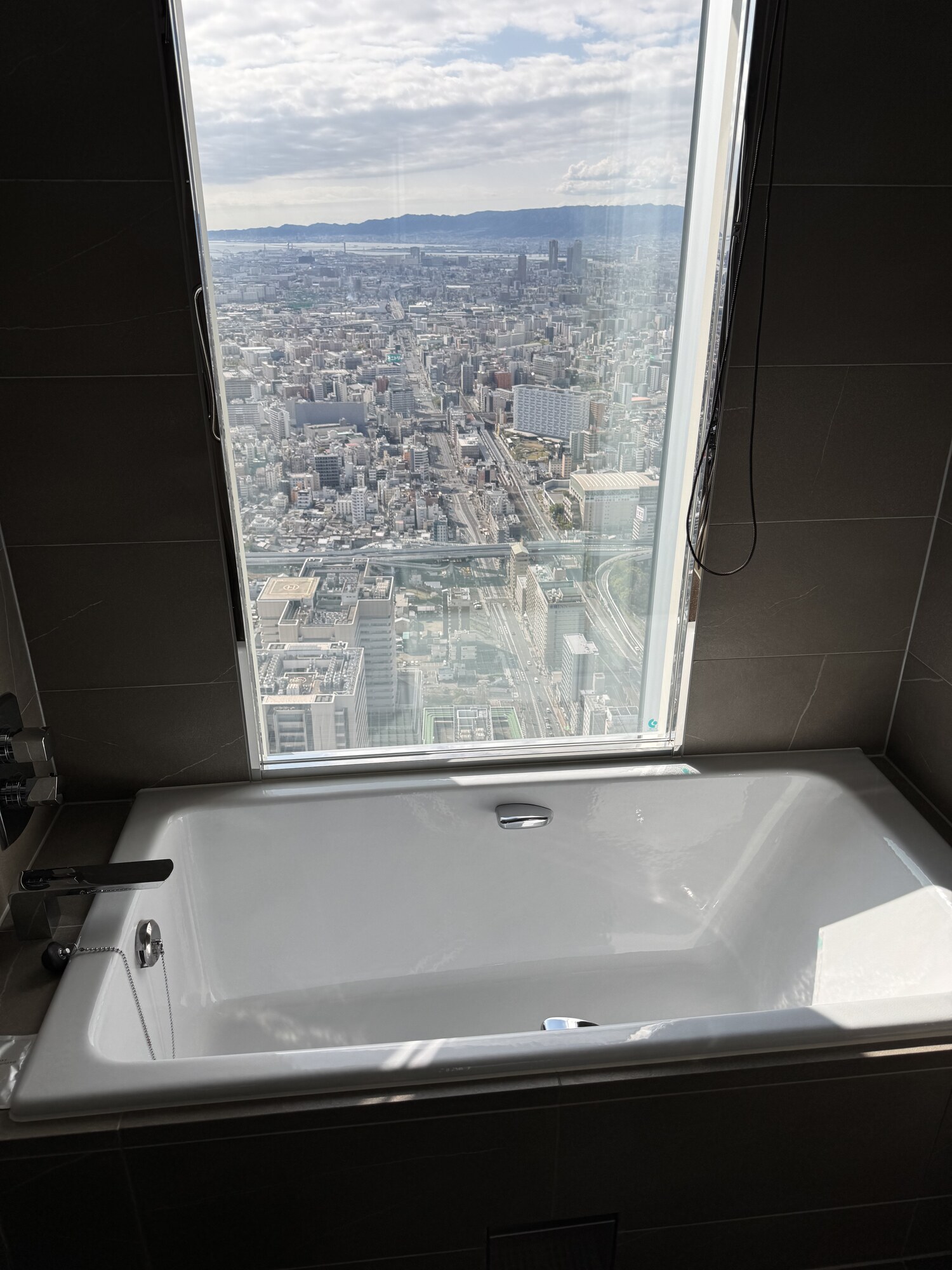 Wanna z widokiem na panoramę Osaki — mokra łazienka z oknem na miasto, wanna przy dużej szybie, wieżowce Osaki w tle