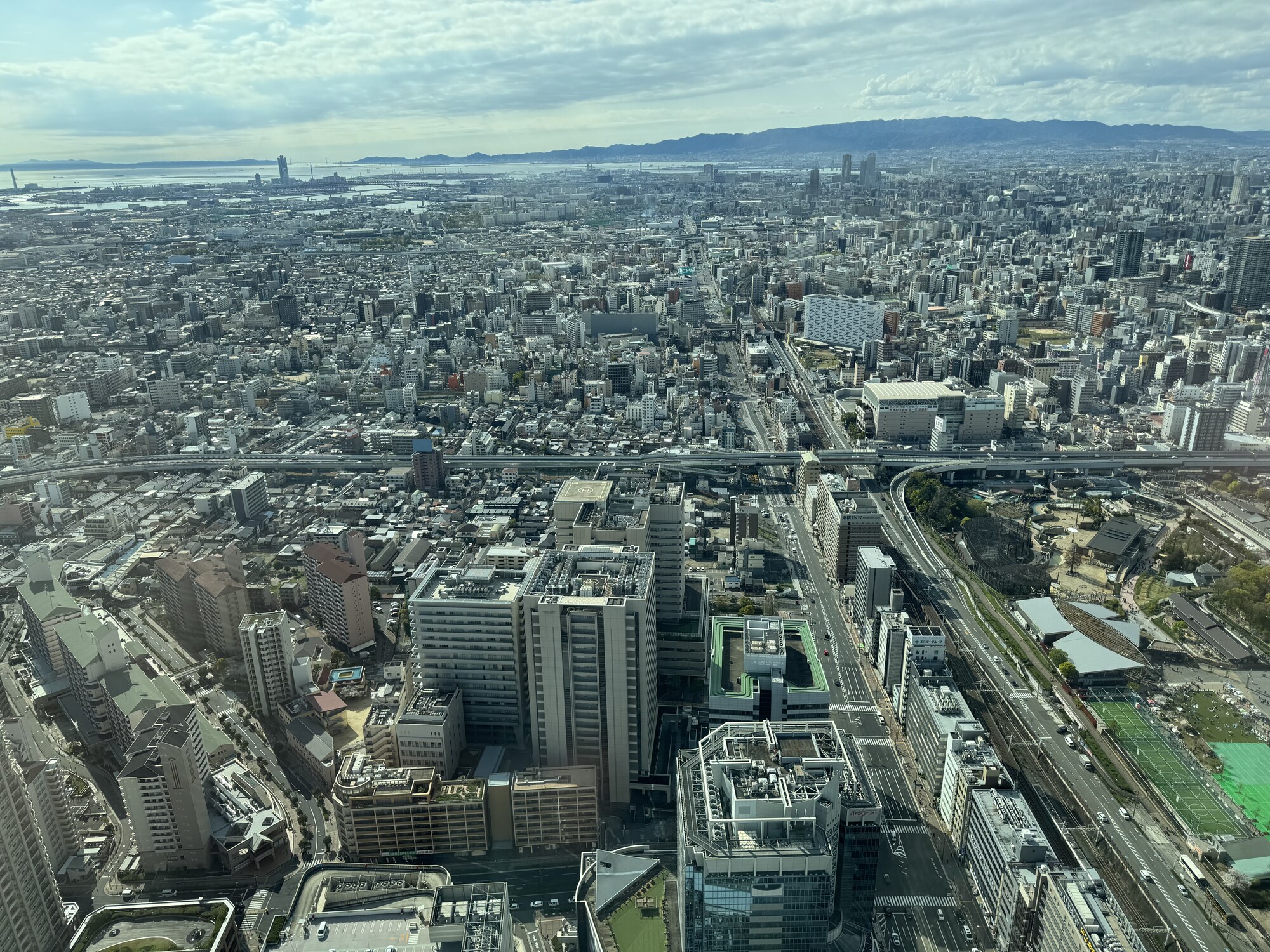 Szeroka panorama Osaki z okna hotelu — miasto po horyzont, w tle góry Ikoma, błękitne niebo