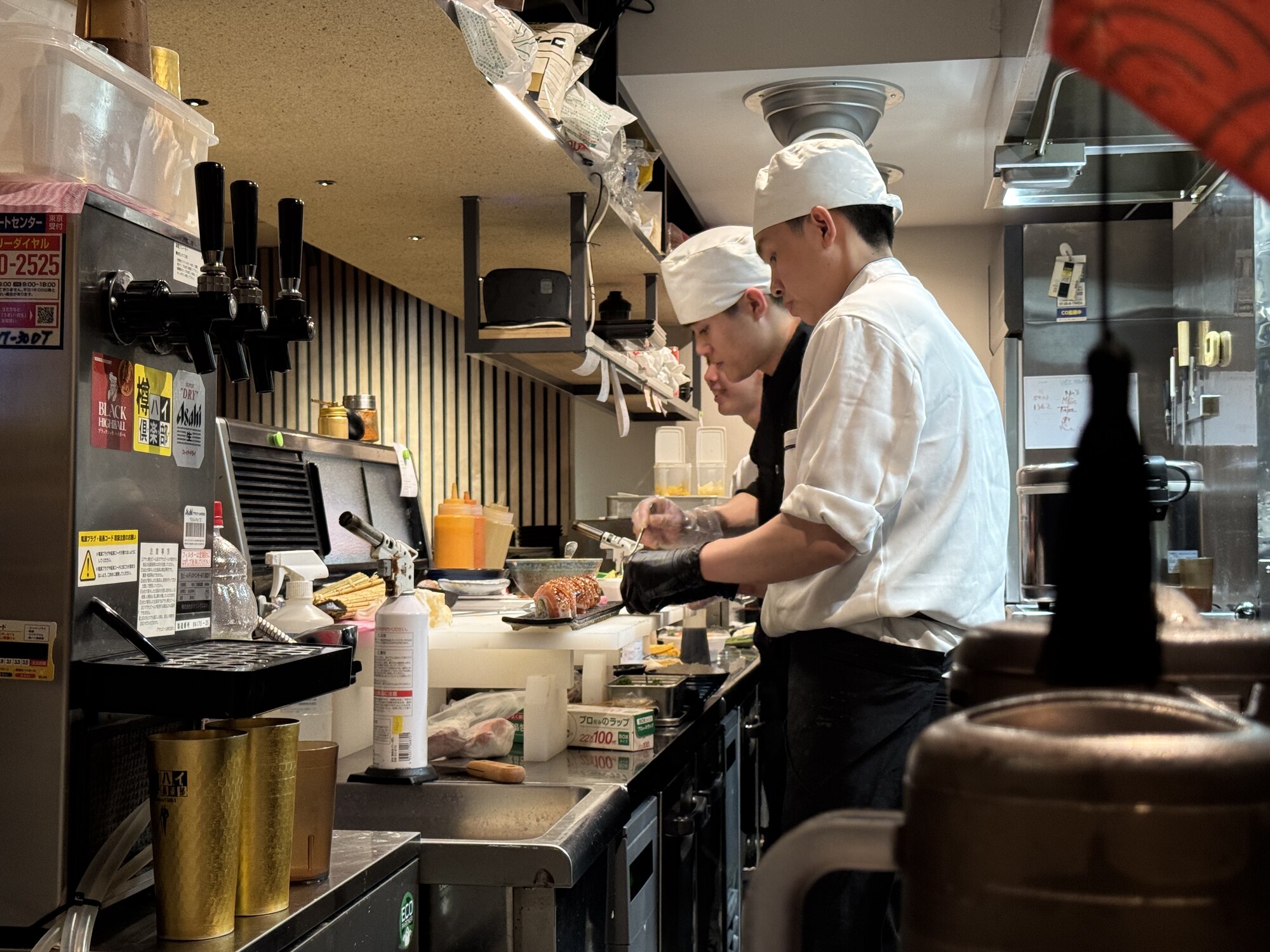 Dwóch kucharzy przy otwartej kuchni japońskiej — para szefów kuchni przy ladzie, świeże składniki, menu za plecami