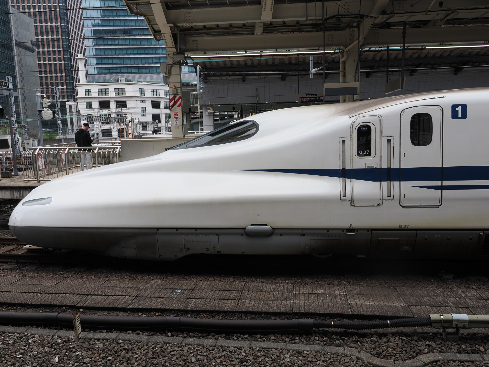 Nos Shinkansena N700S na peronie Tokyo Station — aerodynamiczny dziób, numery wagonów 1, wieżowce w tle