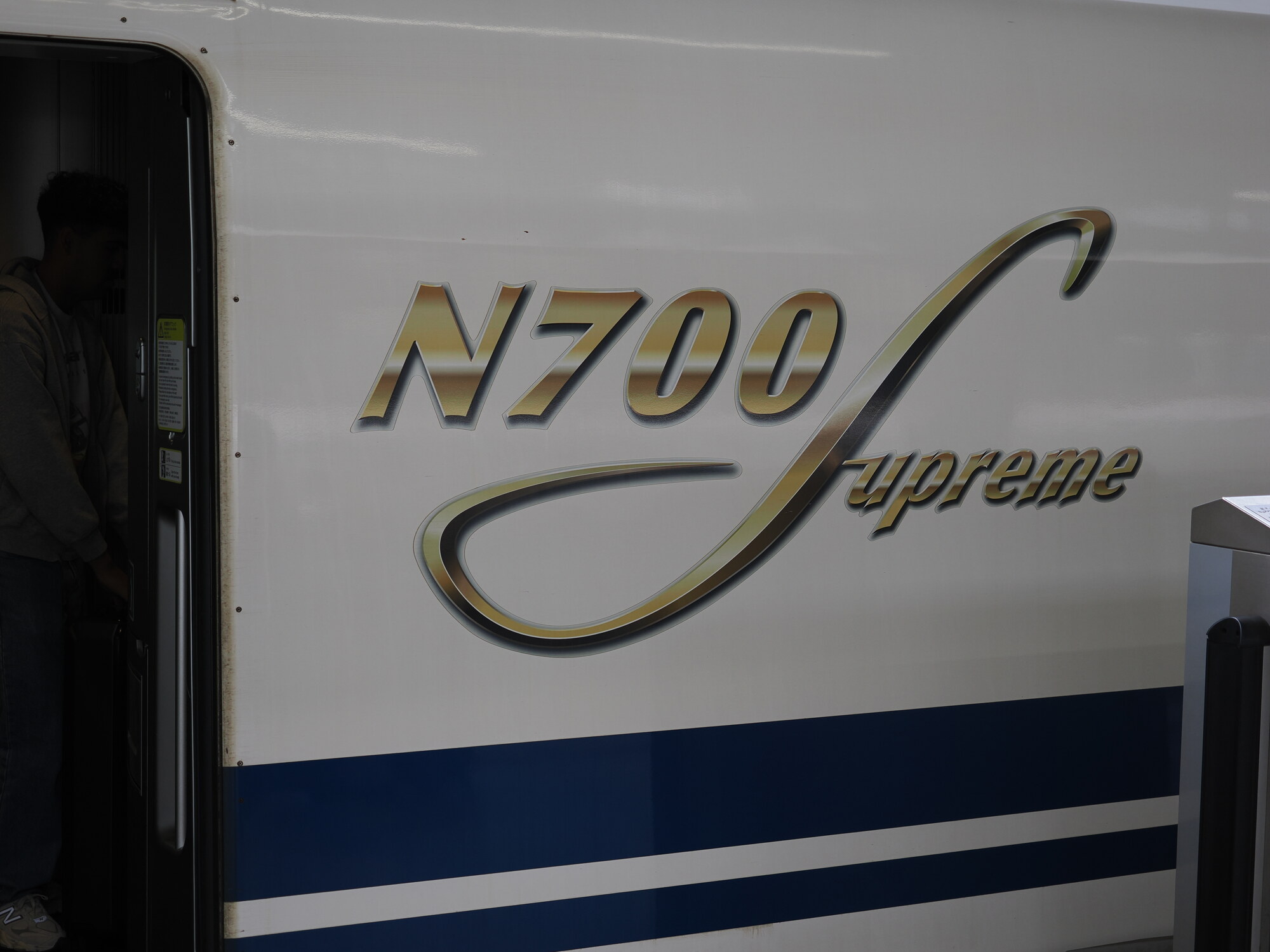 Logo N700 Supreme na boku Shinkansena — złote litery N700S na białym lakierze przy otwartych drzwiach