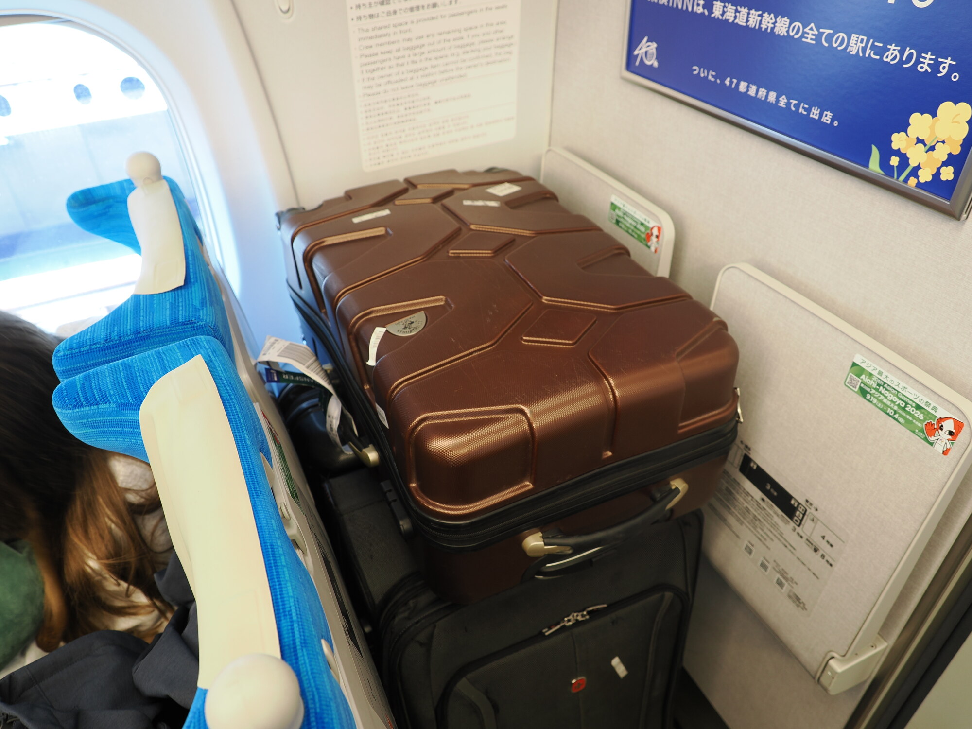 Wnętrze Shinkansena — walizki w przedziale bagażowym za ostatnim rzędem, niebieskie fotele, reklama Super Mario Expo 2026