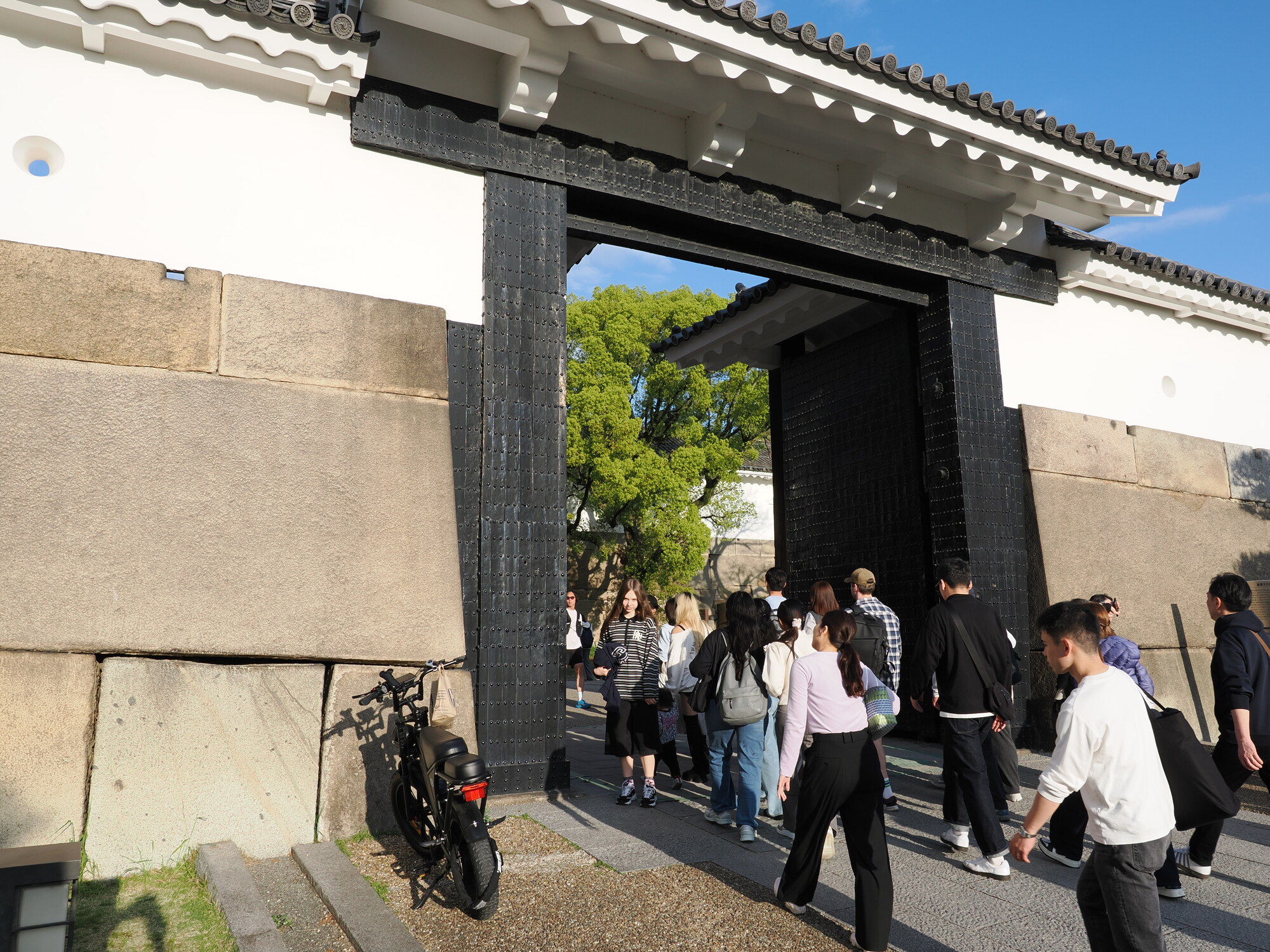 Główna brama zamku Osaka — masywna czarna brama żelazna w białym murze, turyści przechodzący przez wejście