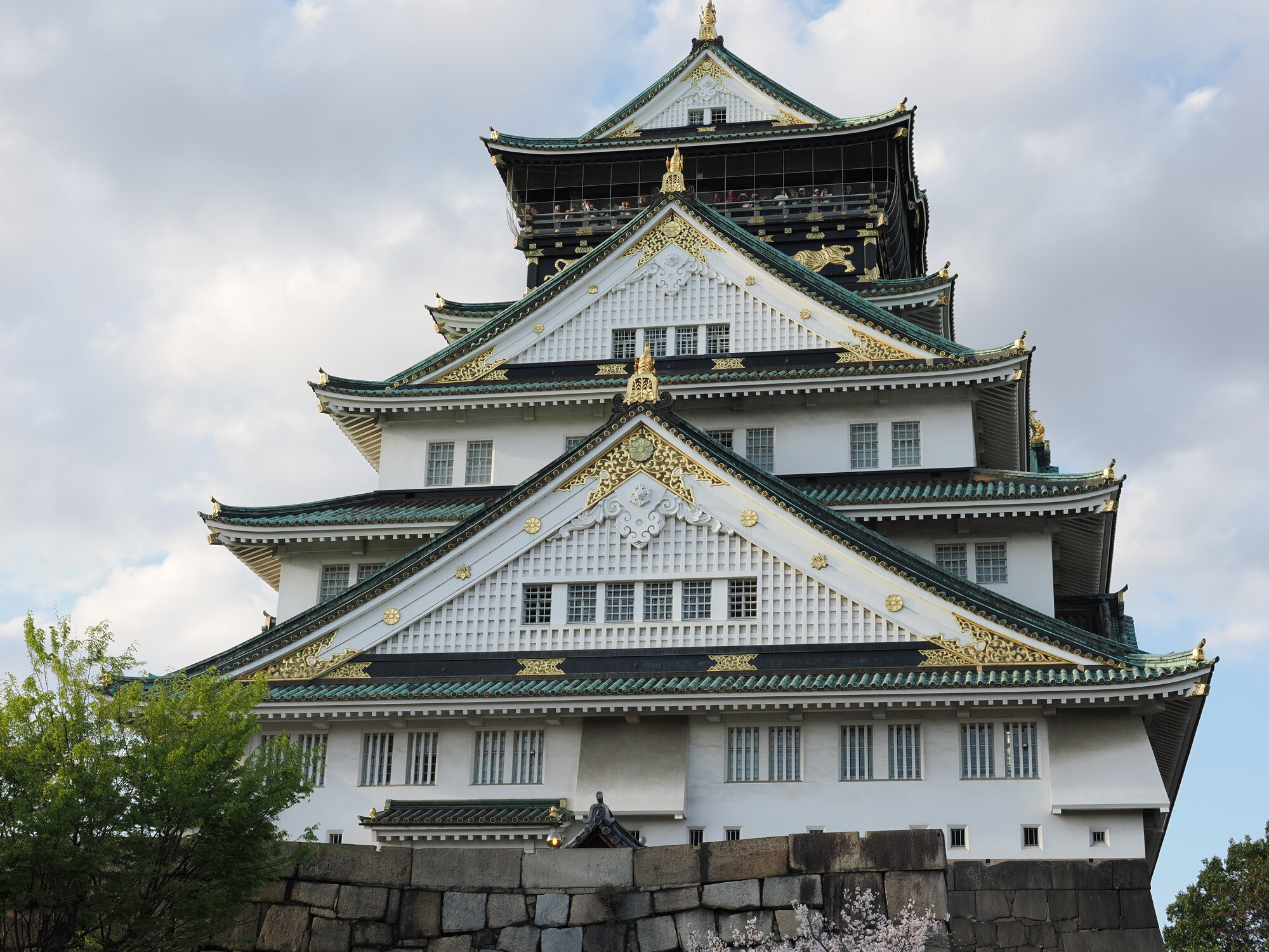 Zamek Osaka z bliska — biała fasada z czarnymi i złotymi zdobieniami na każdej kondygnacji, kamienny fundament