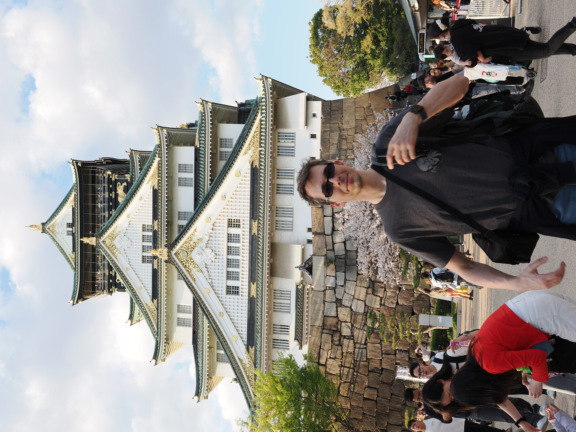 Kamil przed zamkiem Osaka — mężczyzna w okularach contra the castle, wieża za plecami, sakura i tłum