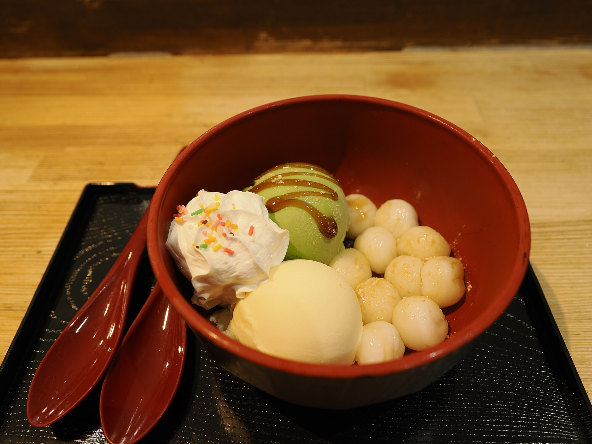 Anmitsu w kawiarni ze zwierzakami — czerwona lakierowana miska z kulkami shiratama mochi, lody matcha, lody waniliowe, bita śmietana i posypka