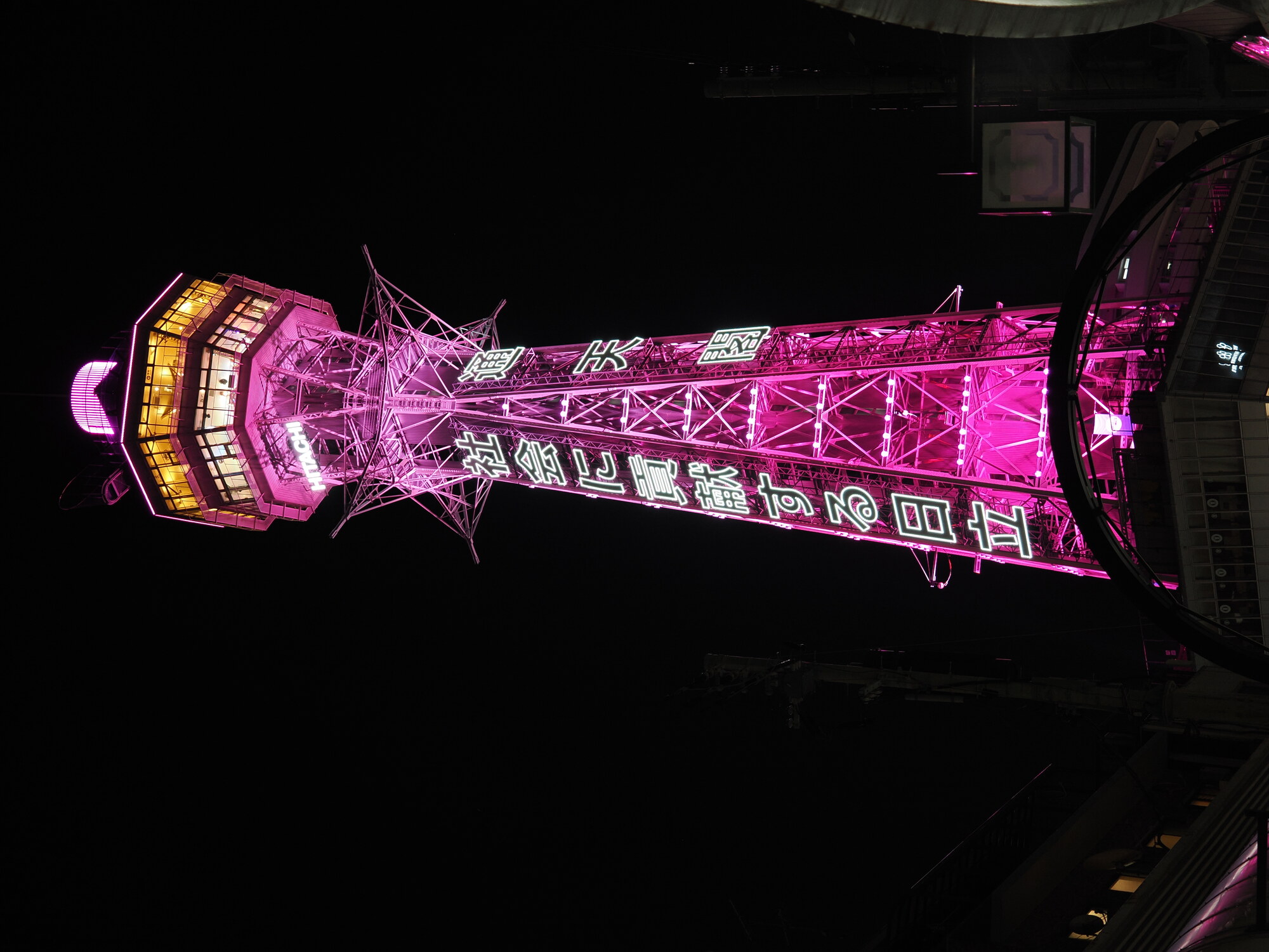 Tsutenkaku z bliska nocą — różowa wieża 103 metry z podświetleniem LED, reklama Hitachi i Tsutenkaku w pełnej krasie, kratownica ze stali