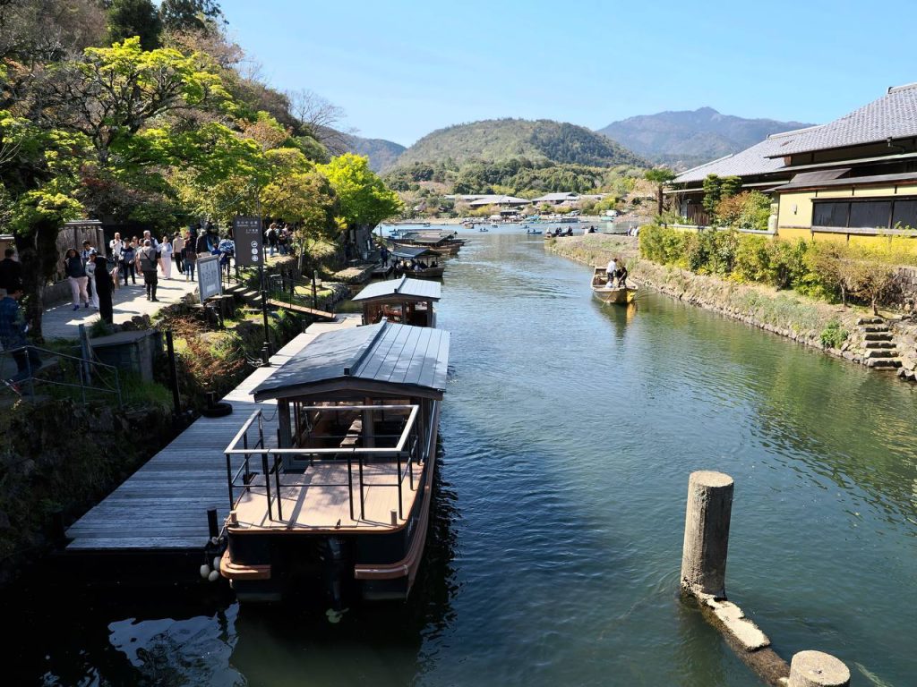 Rzeka Ōi z cumującymi łódkami yakatabune, turystami na nabrzeżu i górą Arashiyama w tle