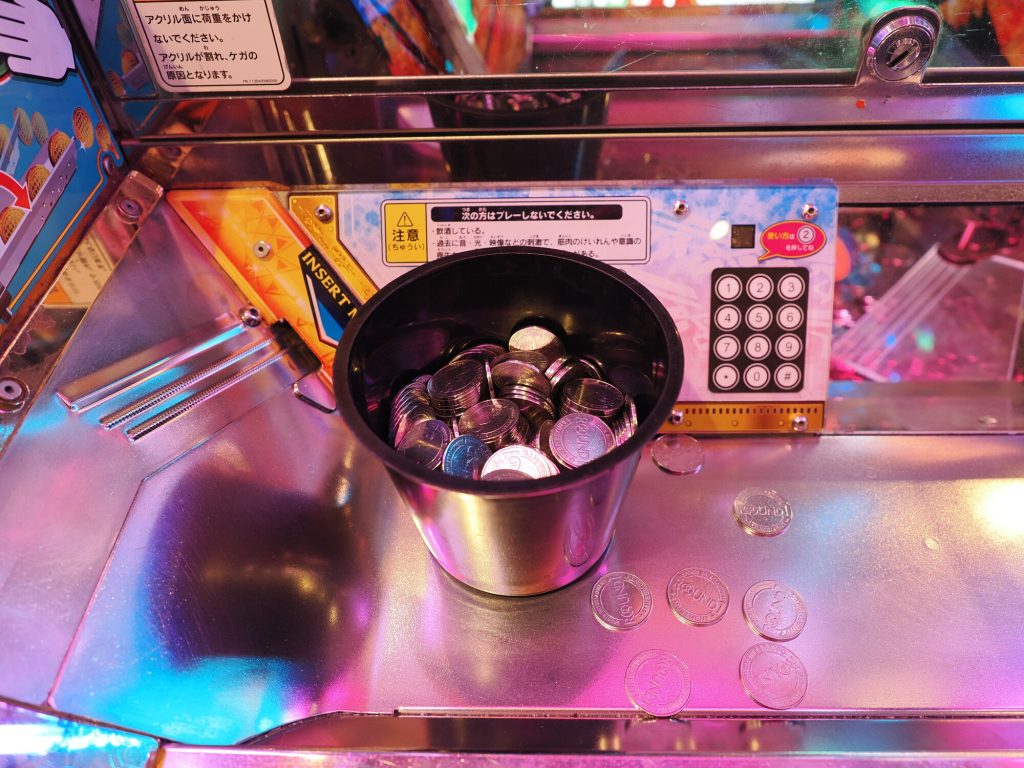 Kubek z żetonami ROUND1 na blacie medal game - srebrne żetony z napisem ROUND, różowe holograficzne oświetlenie