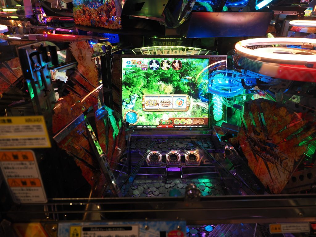 Medal pusher STATION Z w ROUND1 - widok z góry na automat z monetami i ekranem gry dżunglowej Jurassic, niebieskie neony, trzy przyciski START