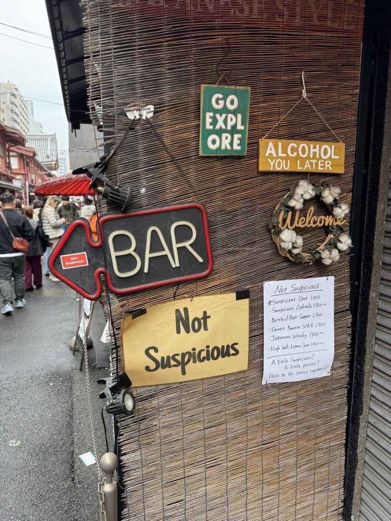 Tokyo Skytree wyłaniające się we mgle nad Asakusą — szyld 雷門東部 Kaminarimon Tobu na pierwszym planie, szyldy sklepów po bokach