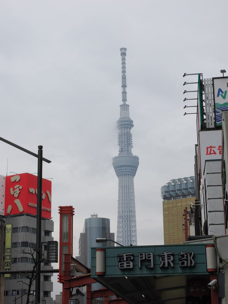 Widok na Solamachi i podstawę Tokyo Skytree od strony kanału — sakura w różowym rozkwicie na pierwszym planie, szyld Sumida Aquarium
